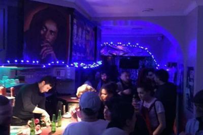 Miniature Location salle Paris 11 (Paris) - Bar de l'Hôtel de la Paix #3 Façade d'un café avec une table extérieure en bois, revêtement en gazon synthétique et intérieur éclairé visible.