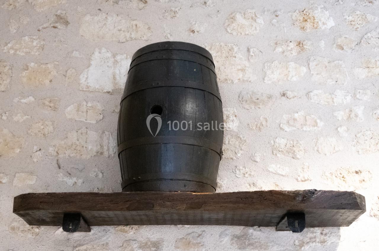 Tonneau en bois sombre posé sur une étagère en bois brut fixée à un mur en pierre claire.
