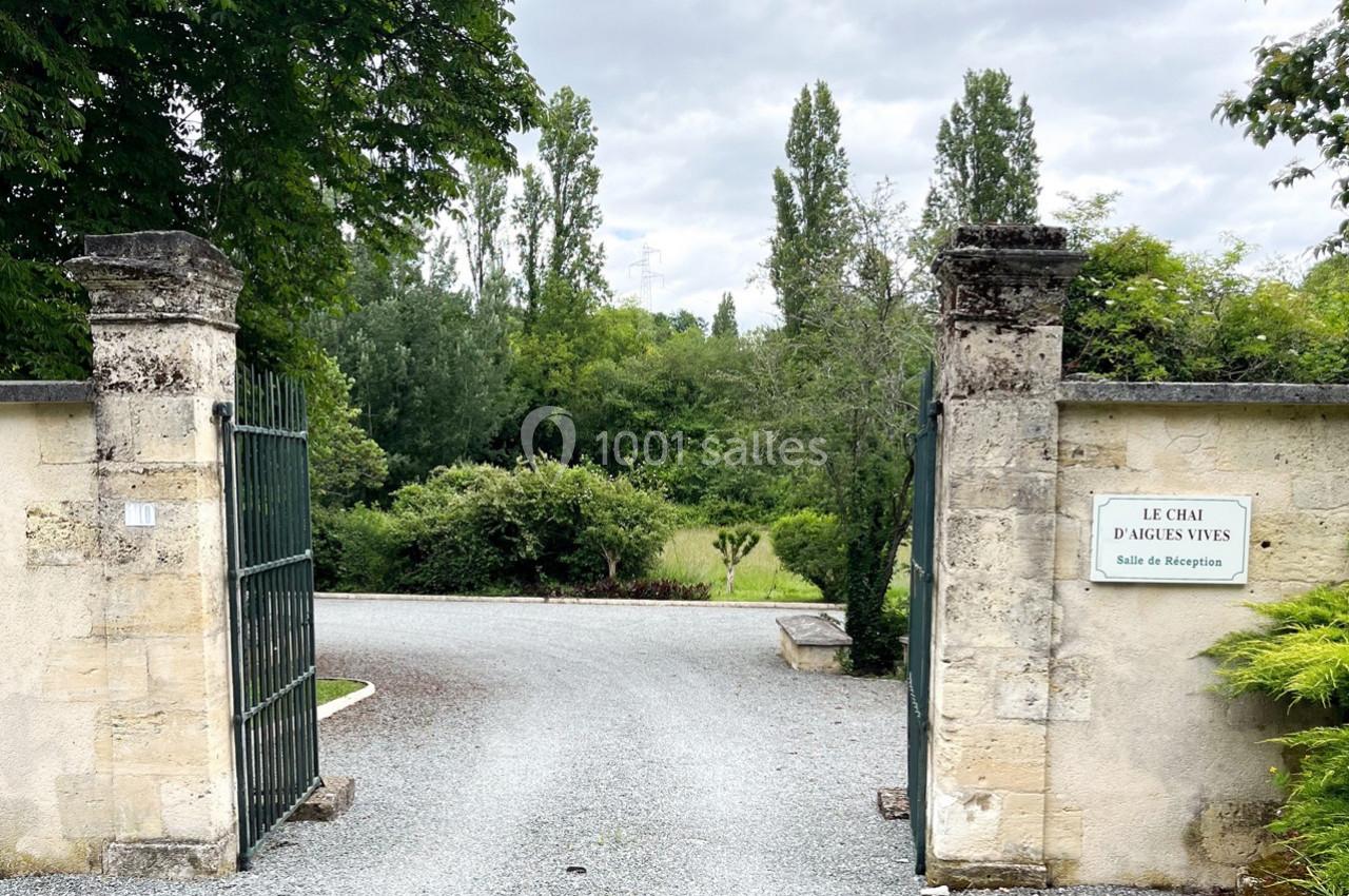 Portail ouvert en pierre avec une allée gravillonnée menant à un espace verdoyant, entouré d'arbres.