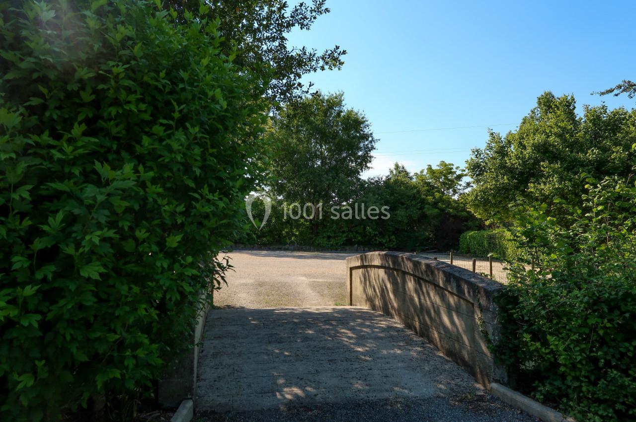 Petit pont en pierre menant à une allée entourée de verdure sous un ciel bleu clair.