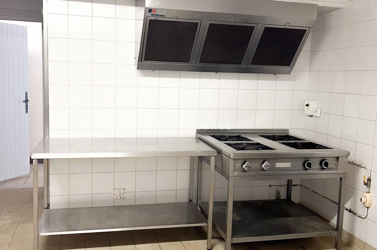 Cuisine professionnelle avec plan de travail en inox, plaque de cuisson à gaz et hotte d'extraction murale.