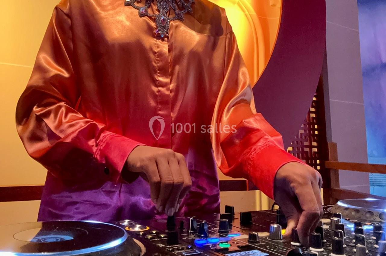 Personne en chemise satinée manipulant une table de mixage dans un environnement lumineux.