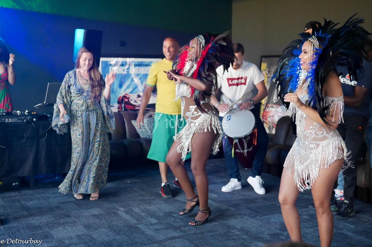 Des danseuses en costumes à plumes colorées exécutent une performance devant un public dans une ambiance festive.