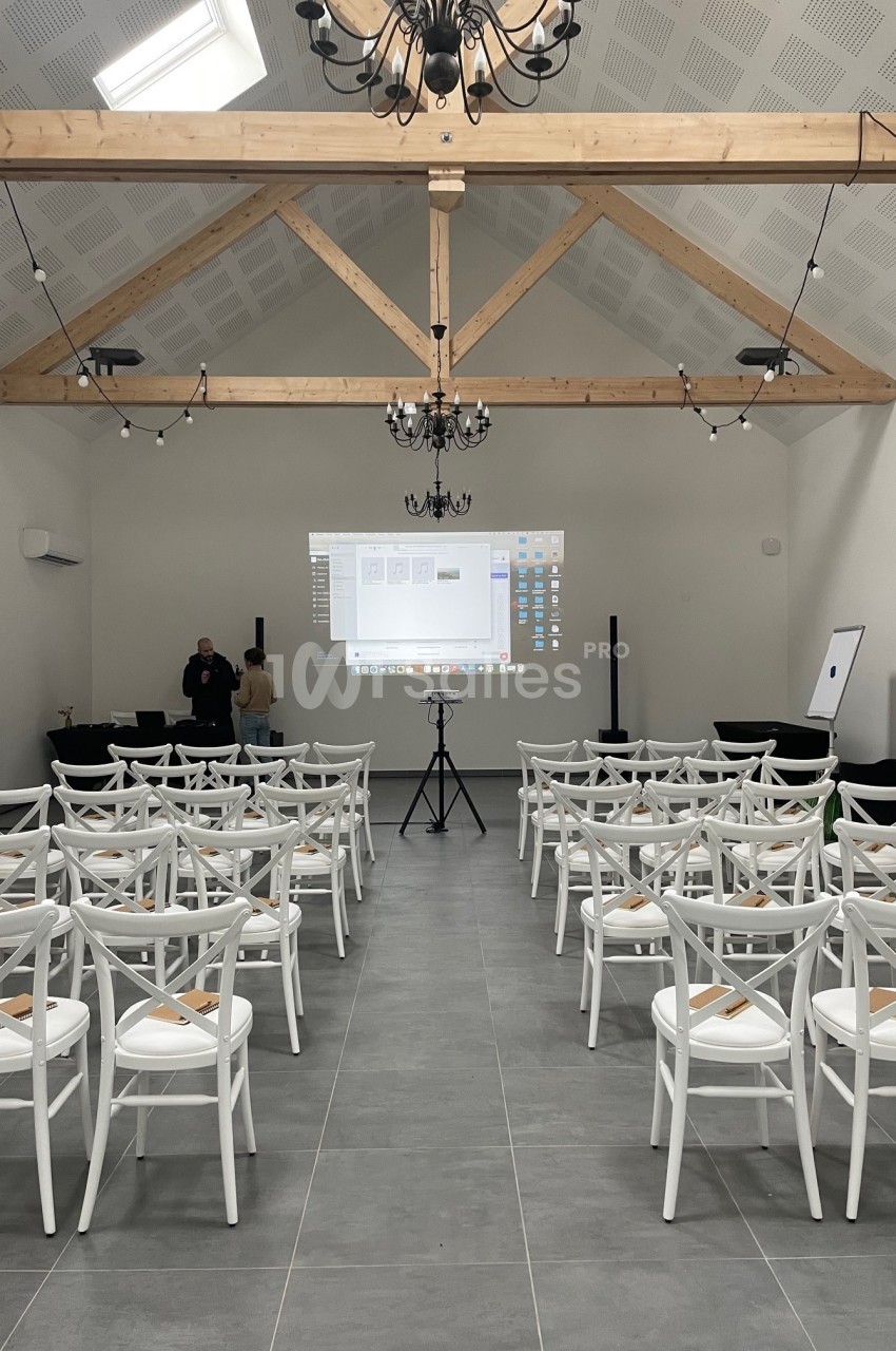 Salle de conférence lumineuse avec des chaises blanches alignées face à un écran de projection allumé.
