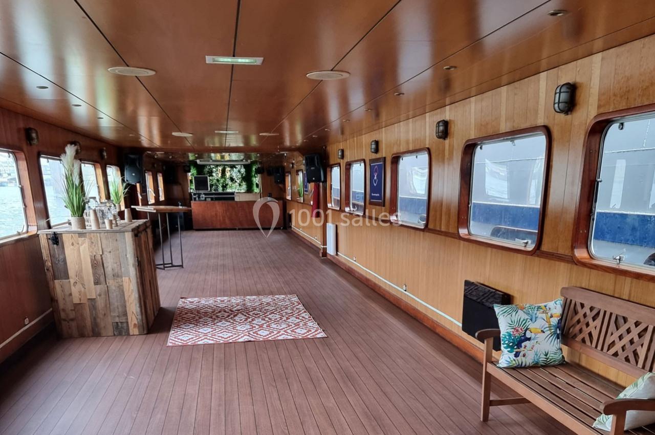 Intérieur d'une péniche aménagée avec un bar en bois, des fenêtres alignées et un espace de détente.