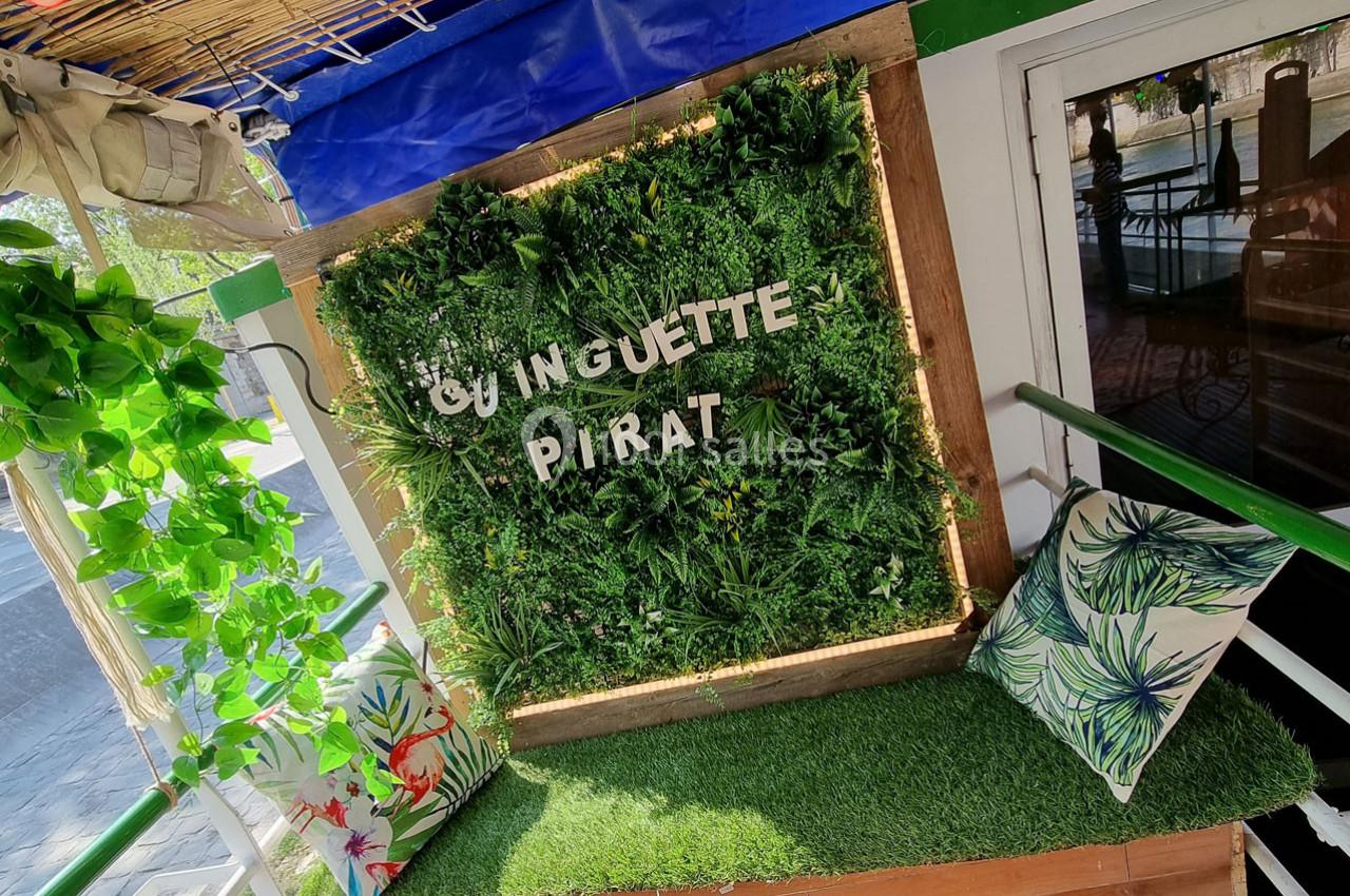 Mur végétal décoratif avec l'inscription ’Guinguette Pirate’, entouré de coussins colorés et d'une végétation luxuriante.
