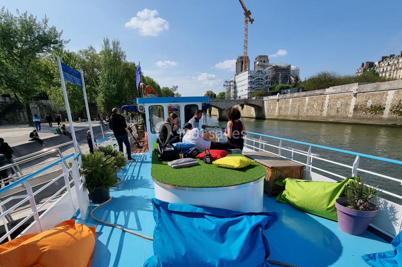 Des personnes assises sur un bateau coloré avec des coussins, naviguant sur une rivière bordée d'arbres et de bâtiments.