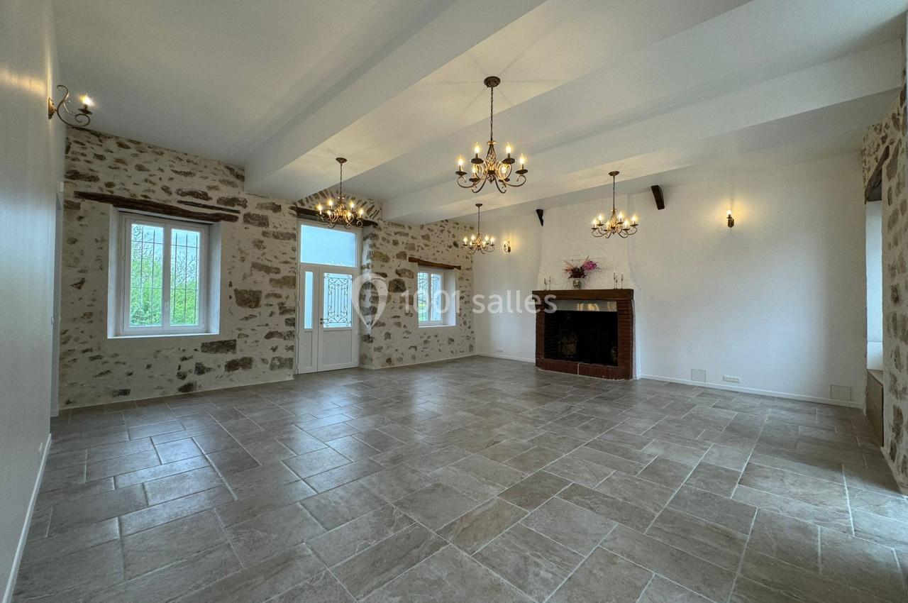 Salle lumineuse avec murs en pierre apparente, carrelage gris, cheminée en briques et lustres suspendus.