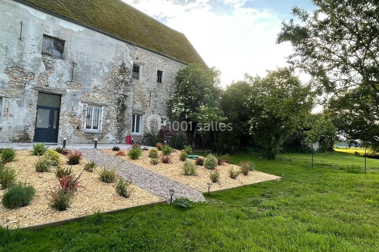 Façade d'une maison en pierre ancienne avec un jardin aménagé de graviers, plantes et allée centrale.
