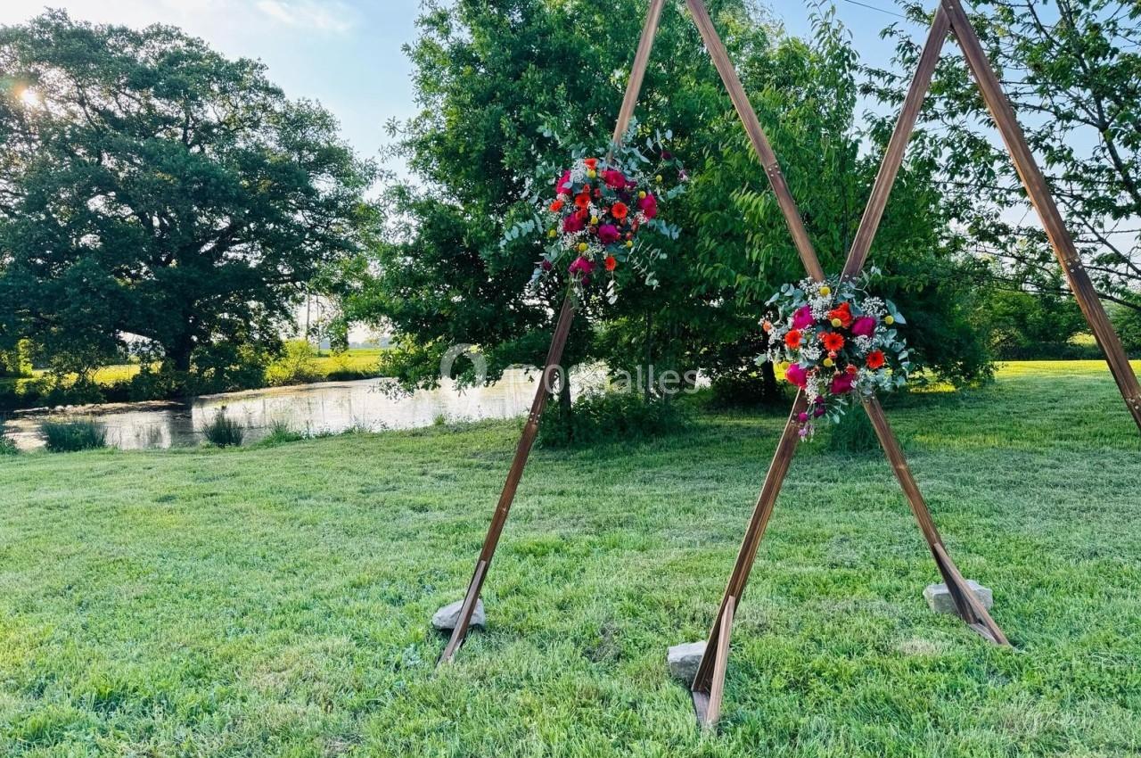 Deux structures en bois triangulaires décorées de bouquets de fleurs colorées sur une pelouse près d'un étang.