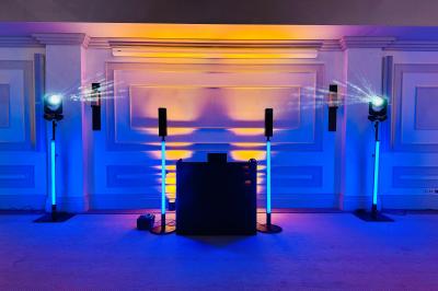 Des invités dansent joyeusement sous des lumières colorées dans une salle décorée pour une fête ou un mariage.