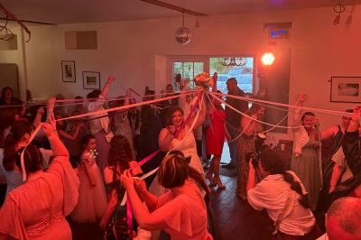 Des invités dansent joyeusement sous des lumières colorées dans une salle décorée pour une fête ou un mariage.