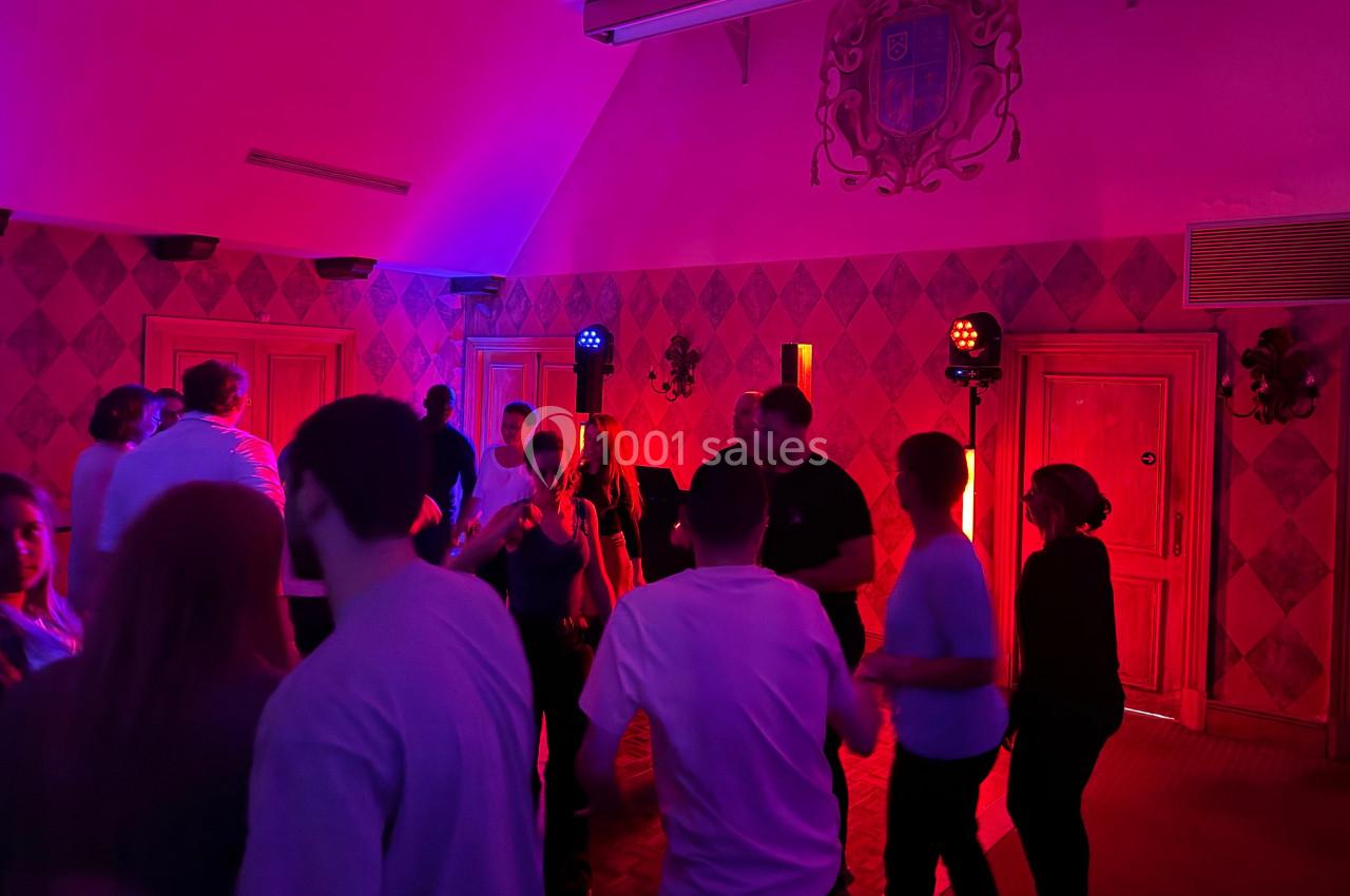 Des personnes dansent dans une salle tamisée éclairée par des lumières colorées, avec un mur décoratif en arrière-plan.