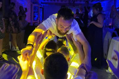 Des invités dansent joyeusement sous des lumières colorées dans une salle décorée pour une fête ou un mariage.