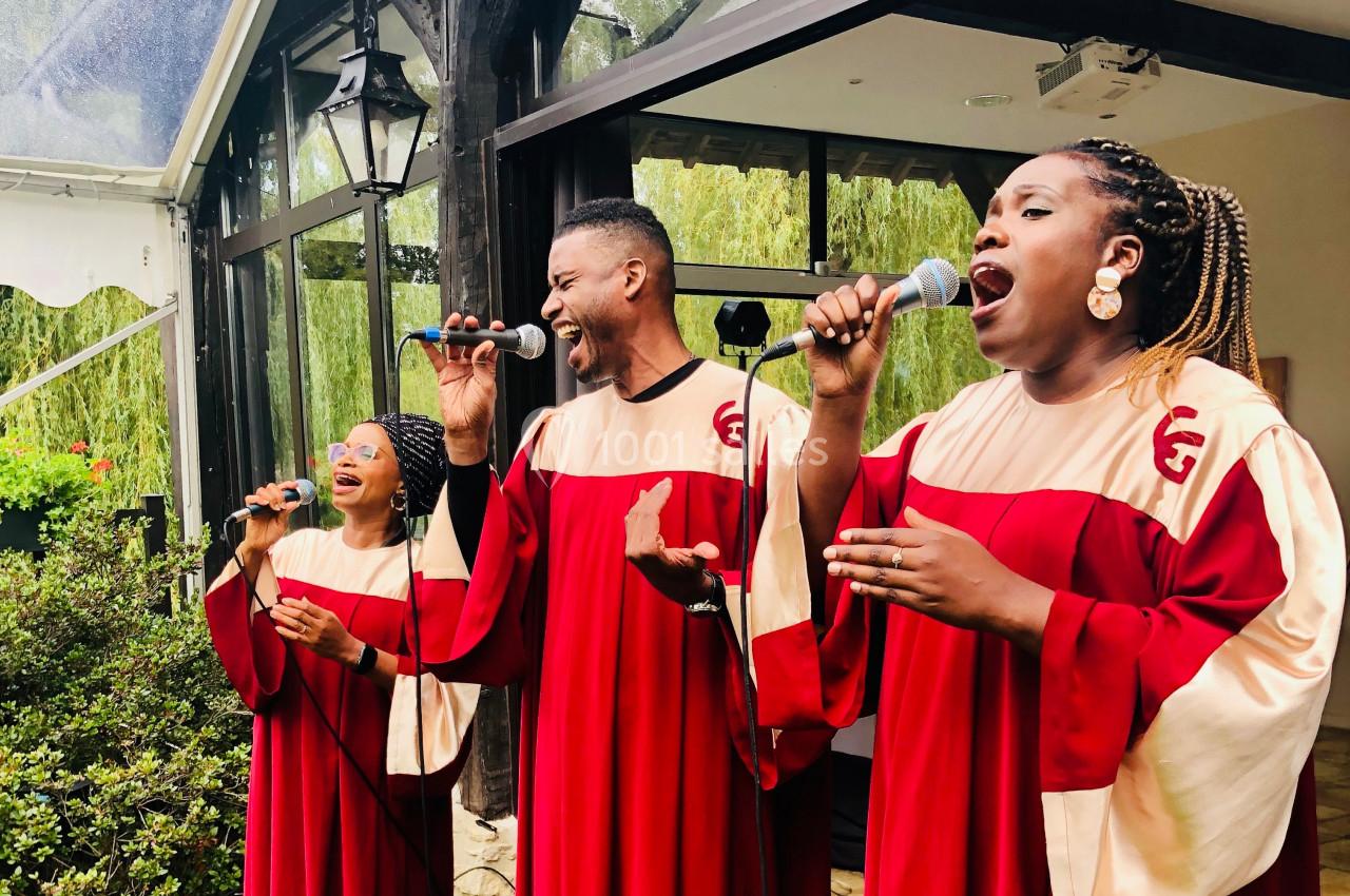 Des chanteurs en tenue de chœur rouge et beige interprètent une chanson avec des micros en extérieur.