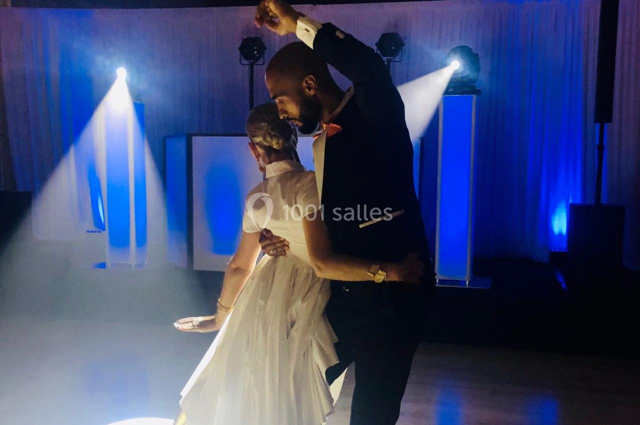 Un couple danse élégamment sous des lumières bleues et blanches dans une salle sombre.
