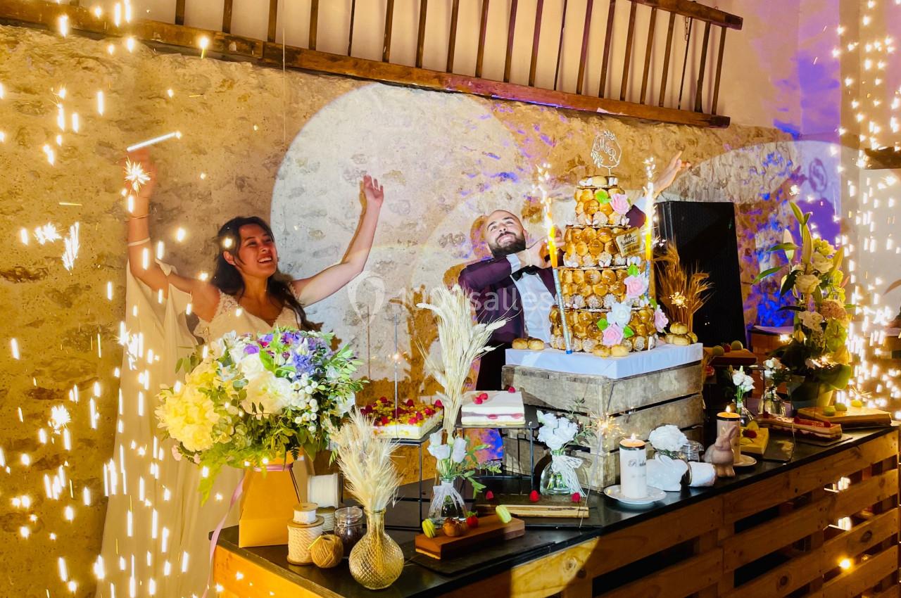 Un couple célèbre leur mariage devant une pièce montée entourée de décorations florales et d'étincelles festives.