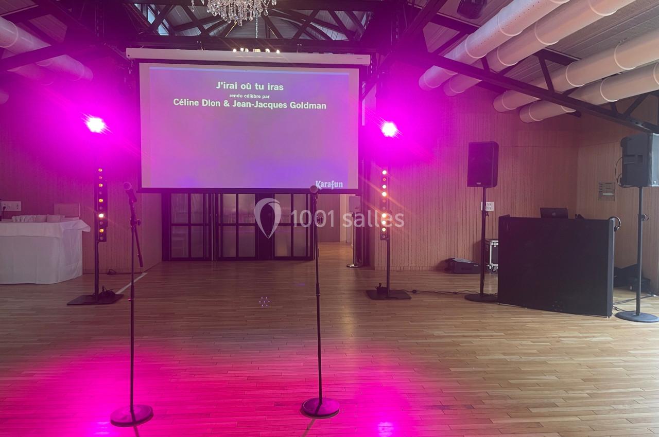 Écran de karaoké affichant les paroles de ’J'irai où tu iras’ dans une salle éclairée par des lumières roses.