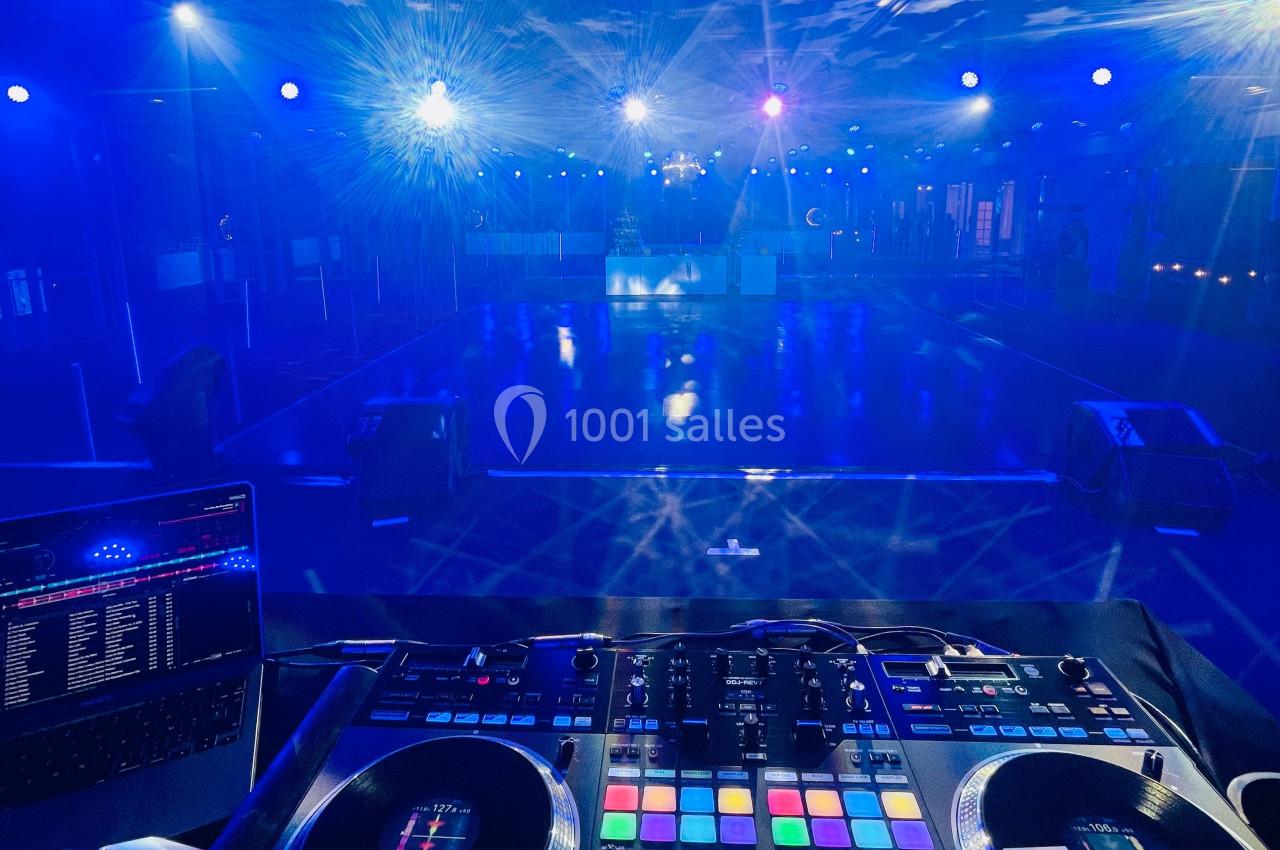 Vue depuis une table de mixage DJ éclairée, face à une piste de danse vide sous des lumières bleues.