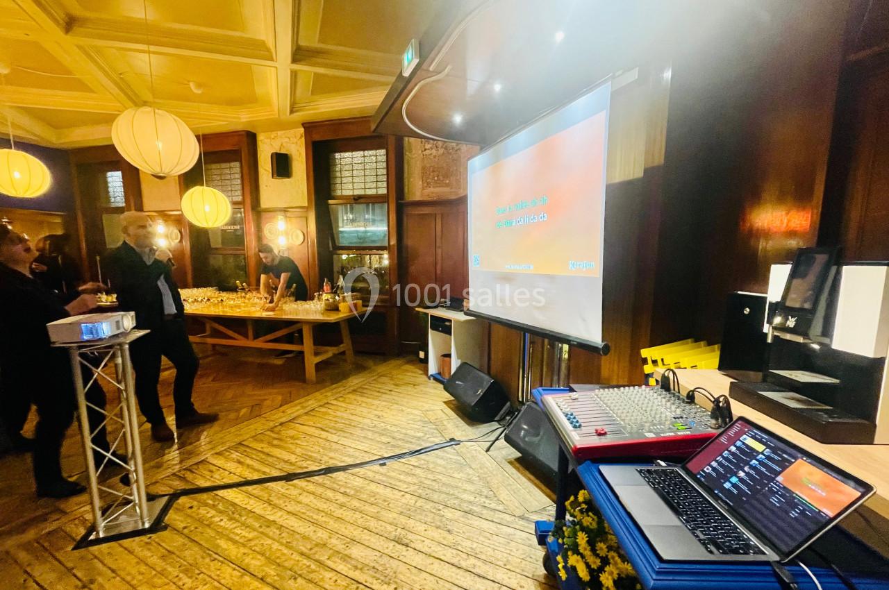 Salle avec parquet en bois, écran de projection, table de buffet éclairée et matériel audio visible au premier plan.