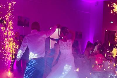 Des invités dansent joyeusement sous des lumières colorées dans une salle décorée pour une fête ou un mariage.