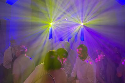 Des invités dansent joyeusement sous des lumières colorées dans une salle décorée pour une fête ou un mariage.