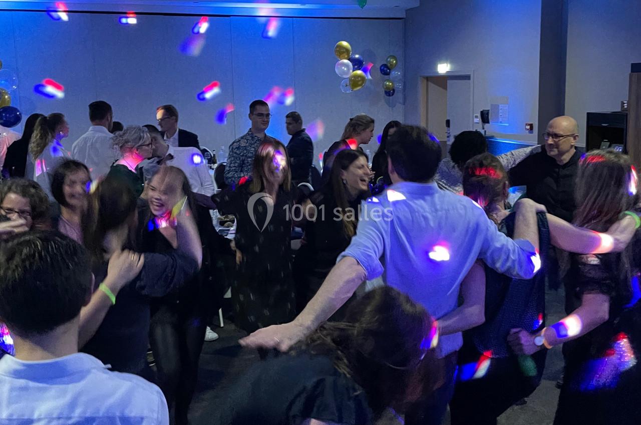 Groupe de personnes dansant dans une salle éclairée par des lumières colorées lors d'un événement festif.