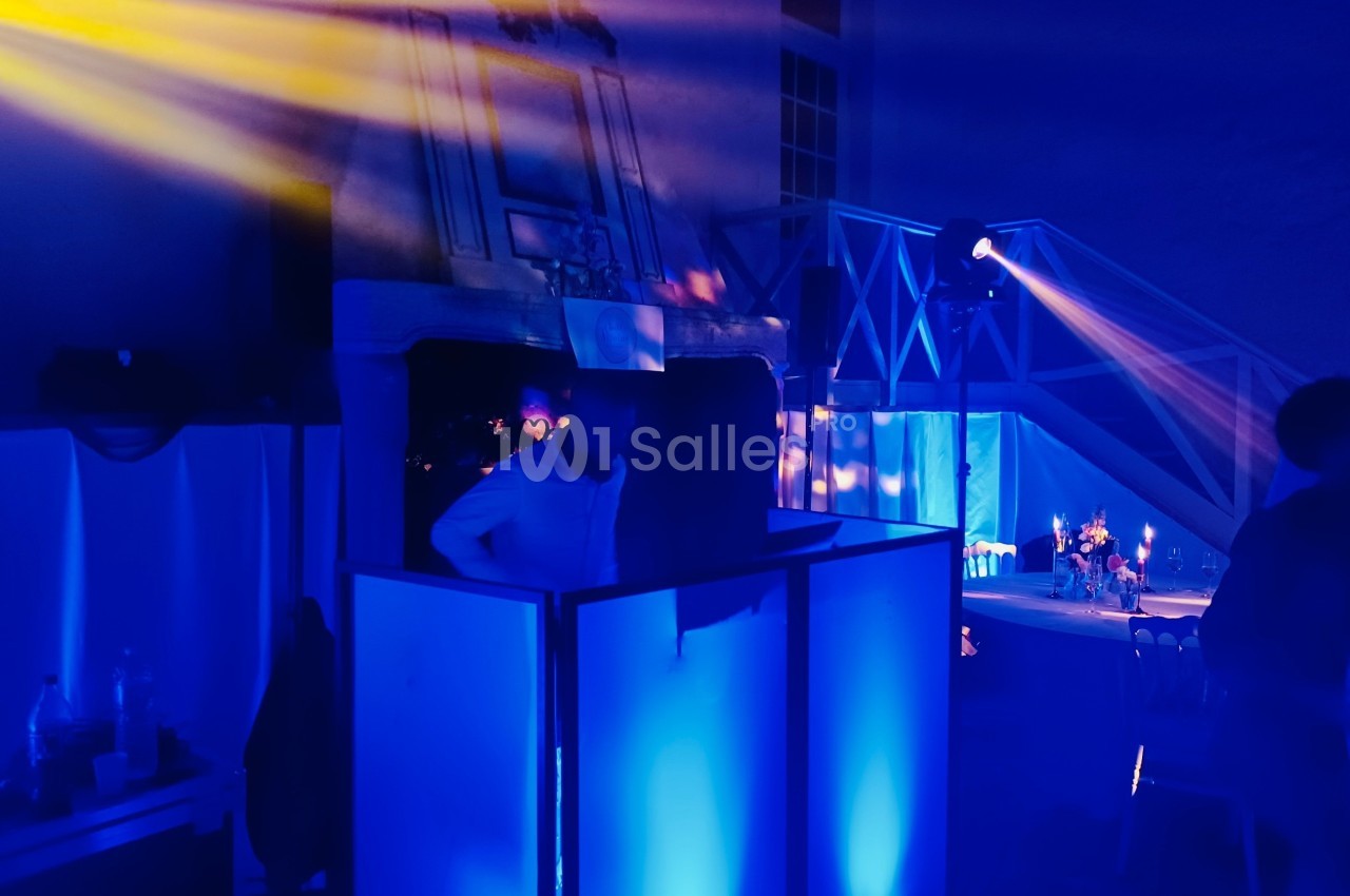 Une personne se tient derrière une console éclairée de lumières bleues dans une ambiance de soirée avec projecteurs colorés.