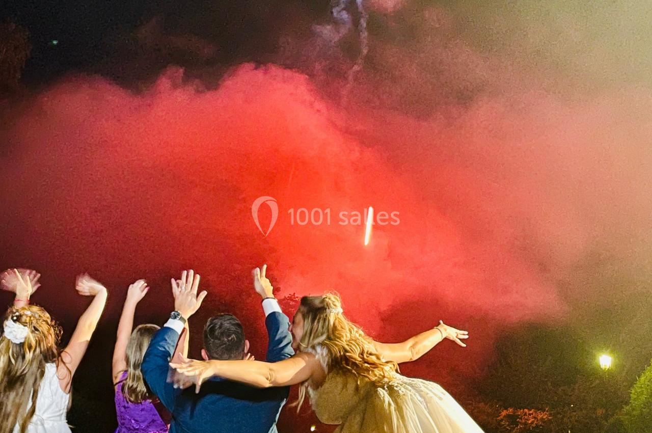 Un groupe de personnes regarde un feu d'artifice illuminant le ciel nocturne avec des fumées rouges.