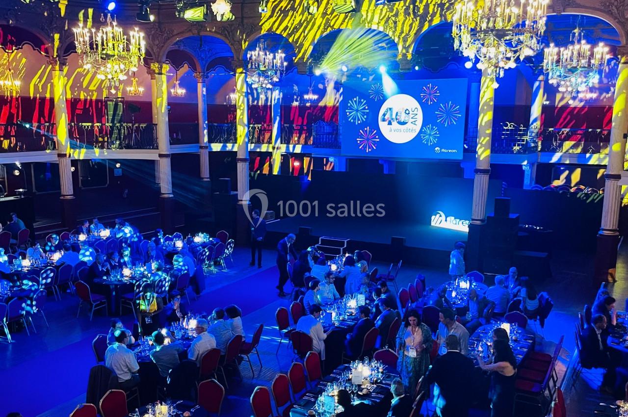 Salle de réception illuminée avec des chandeliers, des projections lumineuses et des invités assis à des tables dressées.