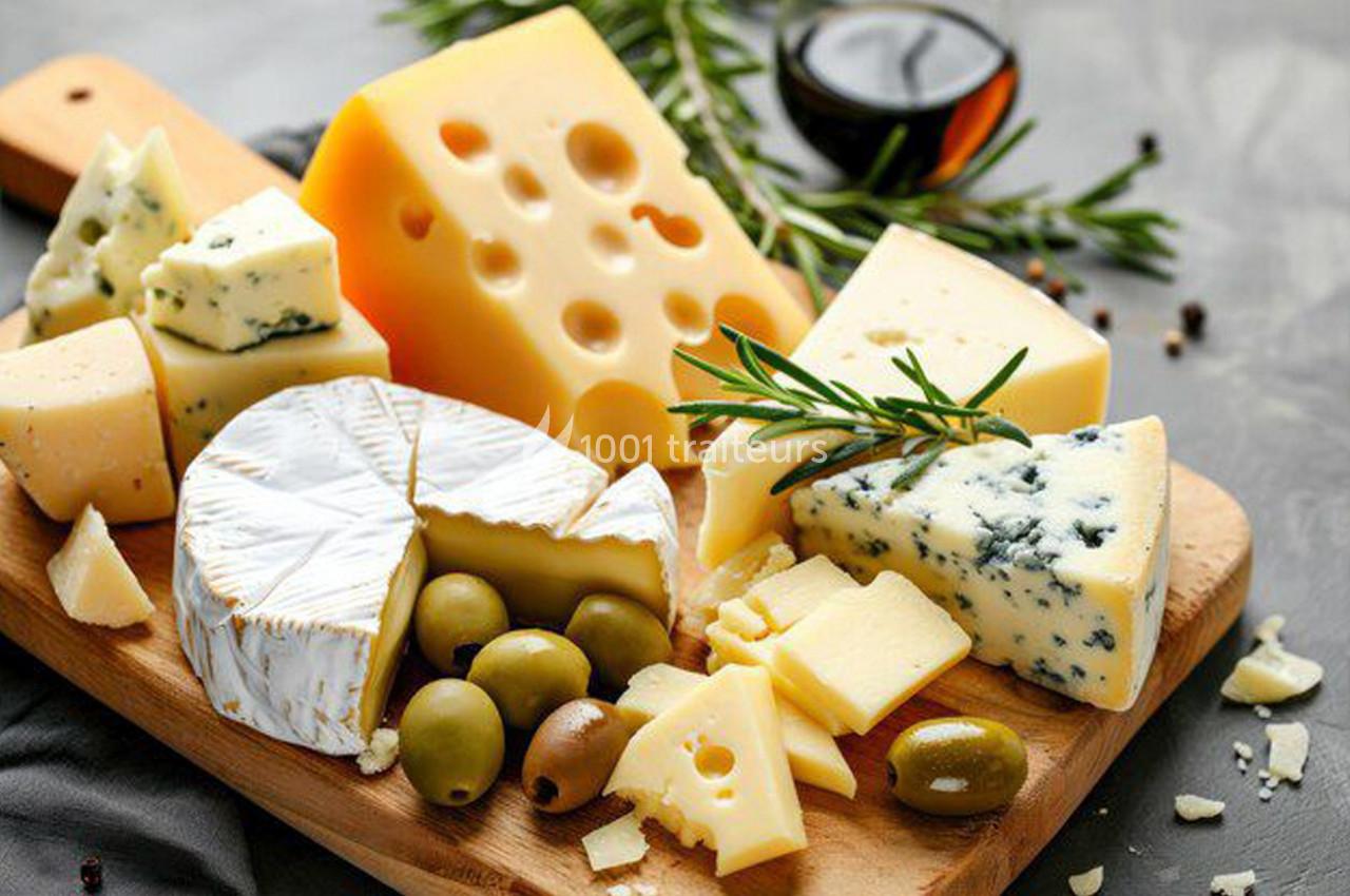 Plateau de fromages variés avec olives, herbes fraîches et une coupelle de sauce en arrière-plan.