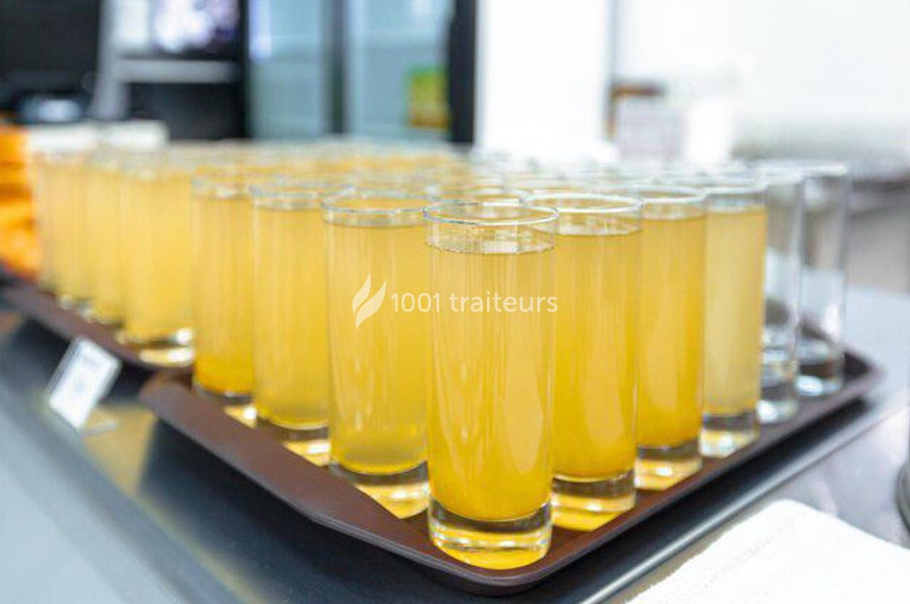 Plateau de verres remplis de jus orange clair alignés sur un comptoir dans un environnement lumineux.