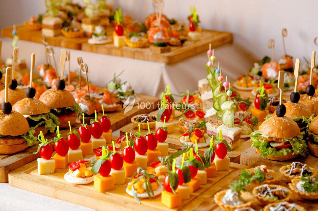 Plateaux de bouchées variées incluant mini-burgers, brochettes de légumes, fromages et canapés sur une table.