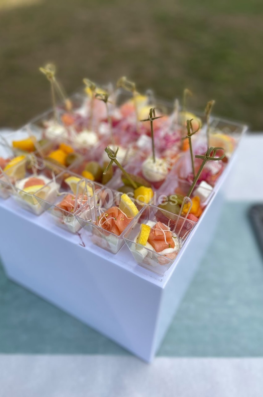 Amuse-bouches en verrines individuelles avec fleurs et herbes aromatiques sur socle blanc.