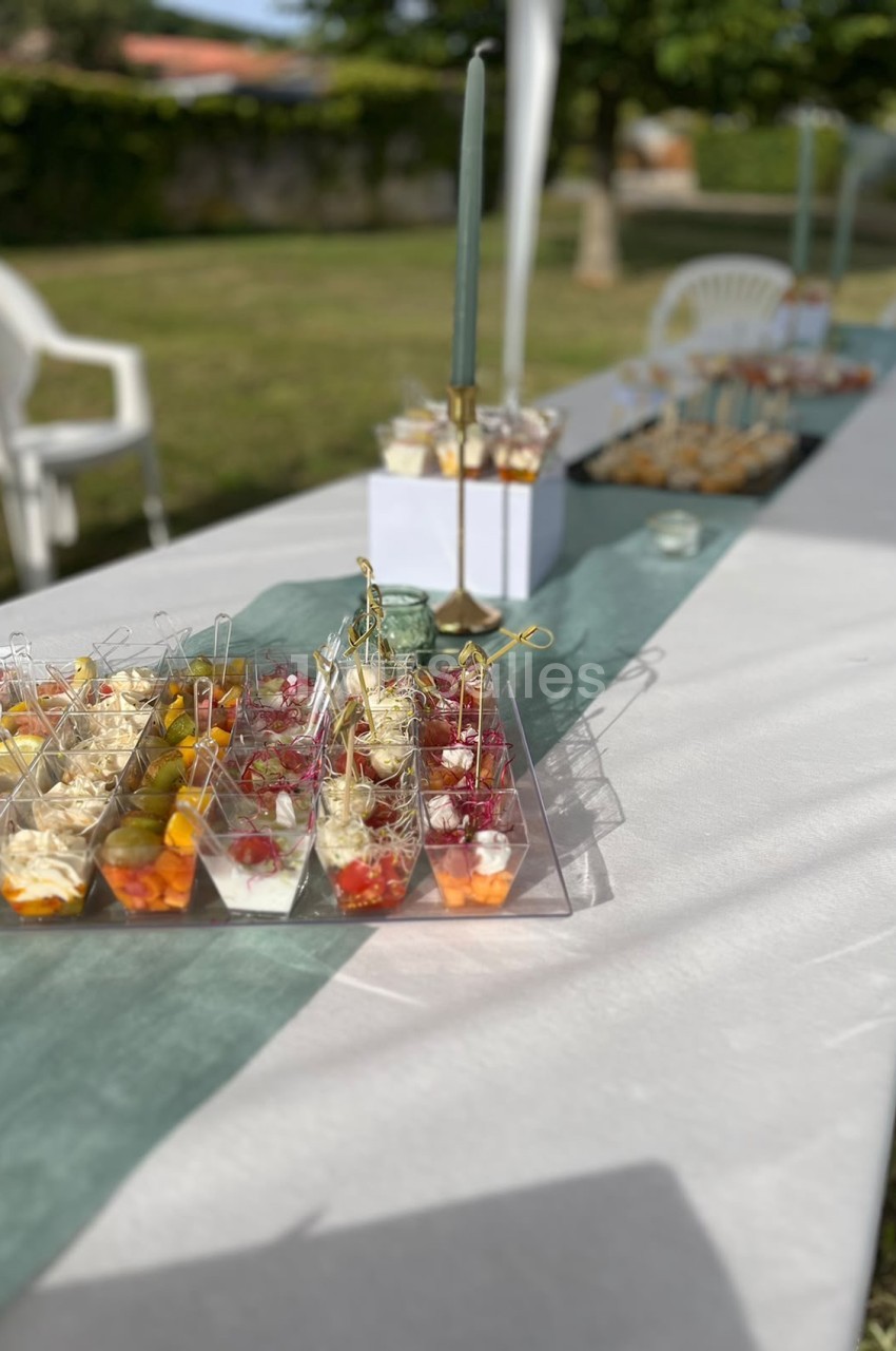 Table dressée en extérieur avec verres de cocktails aux fruits rouges et jaunes, chandelier doré et décoration de table verte.
