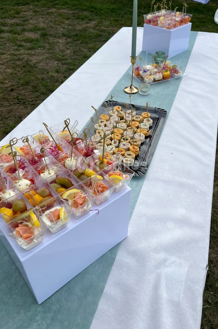 Table dressée en plein air avec plateau de verrines, brochettes, fruits secs et cocktails en verre.