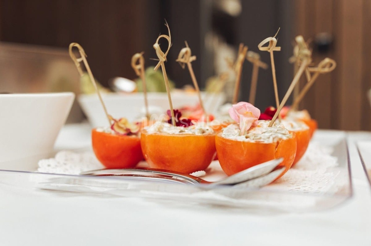 Tomates évidées garnies de crème et piques dorées, décorées de fleurs comestibles sur assiette blanche.