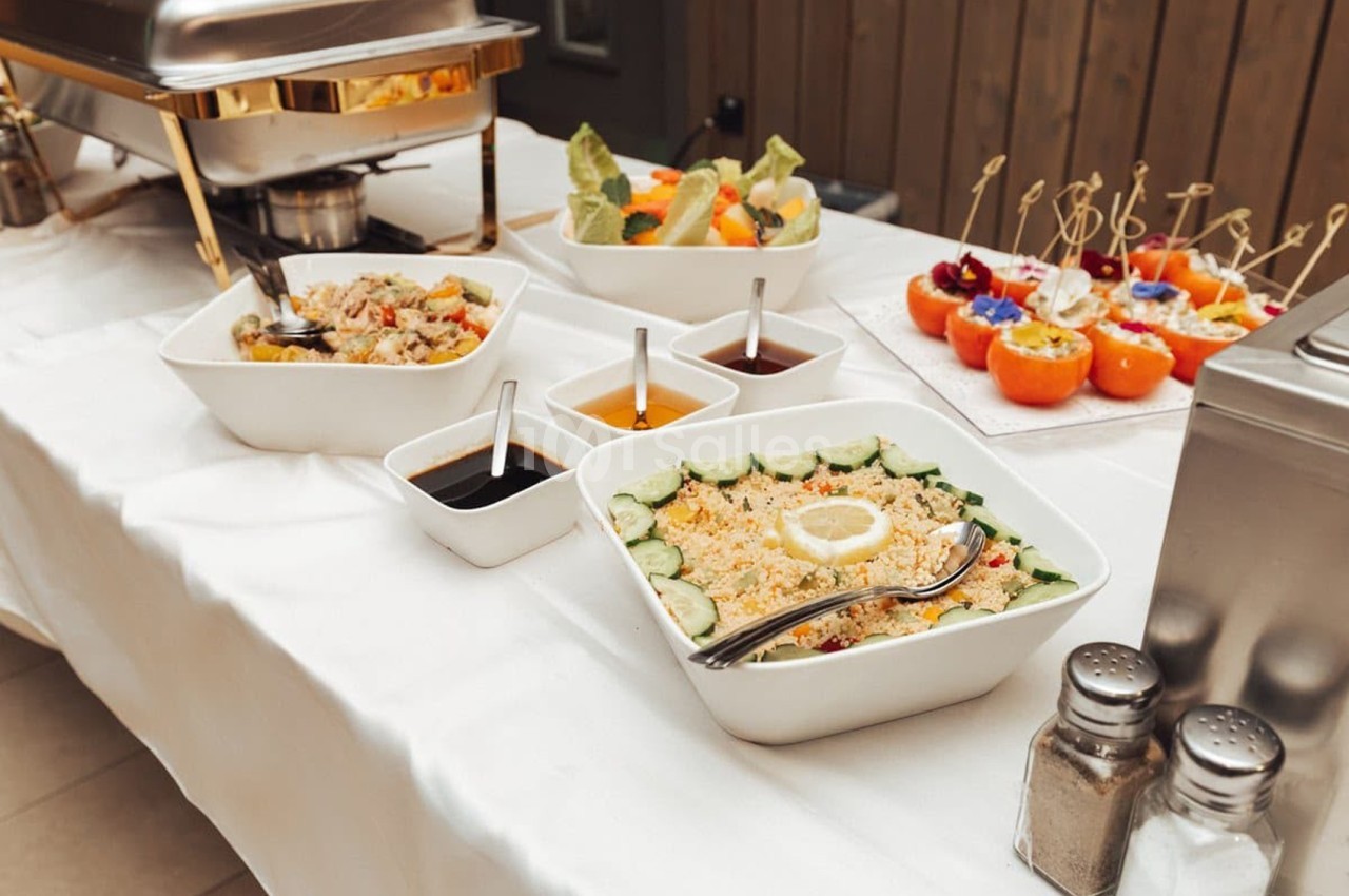 Buffet traiteur avec riz aux légumes, salades, tomates farcies et sauces en bols blancs.
