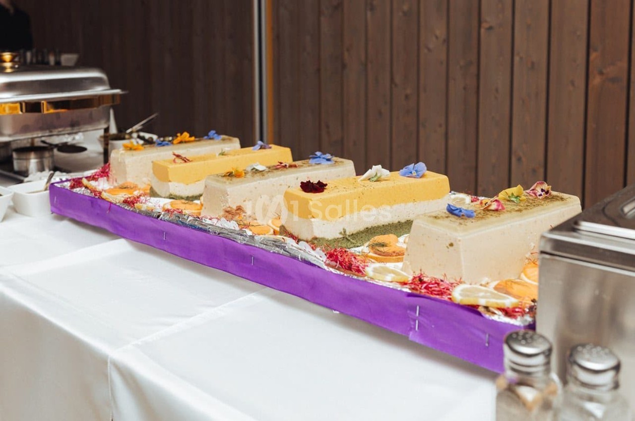 Plateau de cakes individuels garnis de coulis, mousse et fleurs comestibles sur socle violet.