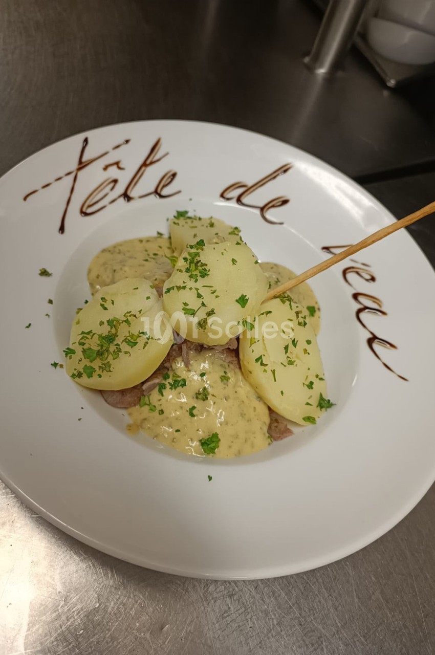 Assiette blanche avec filet de viande, sauce à base de moutarde et tranches de pommes de terre parsemées de persil frais.