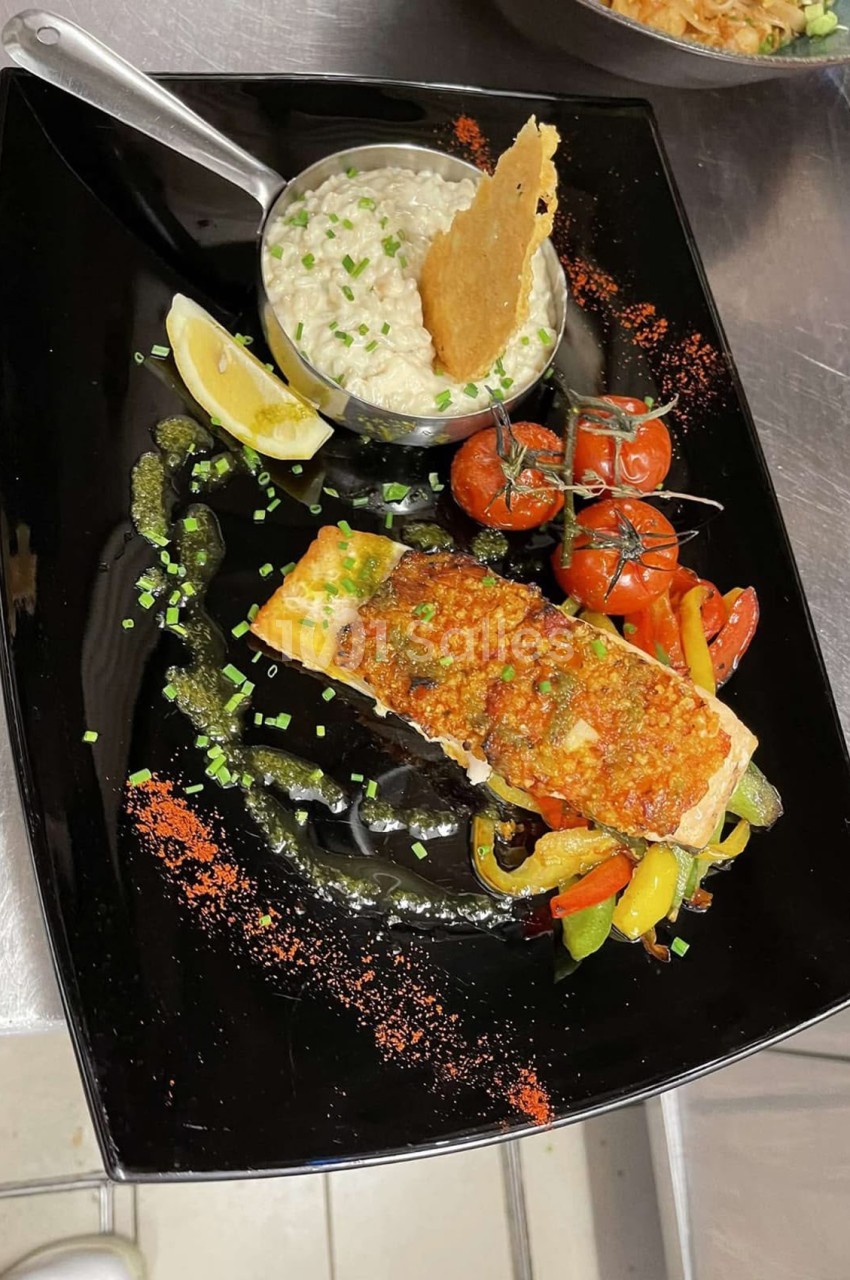 Filet de poisson doré aux légumes grillés - tomates, poivrons - et sauce crémeuse sur assiette noire.
