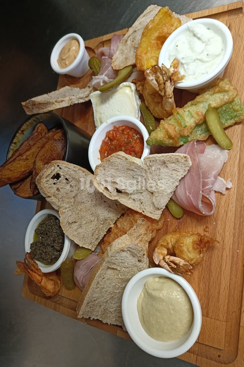 Planche charcuterie composée de pains, charcuterie, cornichons et sauces en ramekins sur bois.