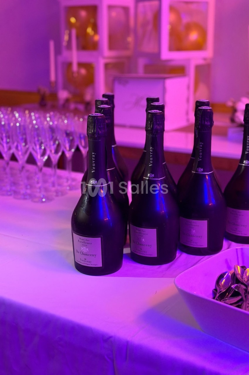 Plusieurs bouteilles de vin mousseux Vouvray sur une table recouverte d'une nappe blanche, éclairée en violet, avec des flûtes à champagne en arrière-plan.
