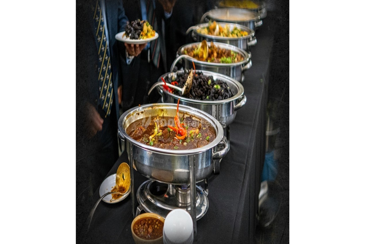 Buffet avec plusieurs plats chauds et froids présentés dans des récipients en inox sur une table noire.