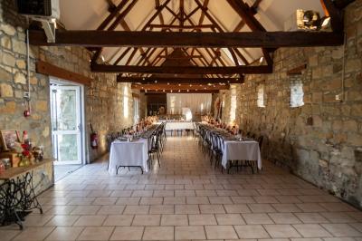 Miniature Location salle Esmery-Hallon (Somme) - La Bergerie #23 Salle de réception en pierre avec tables dressées, décorations florales et bougies, éclairée par la lumière naturelle.
