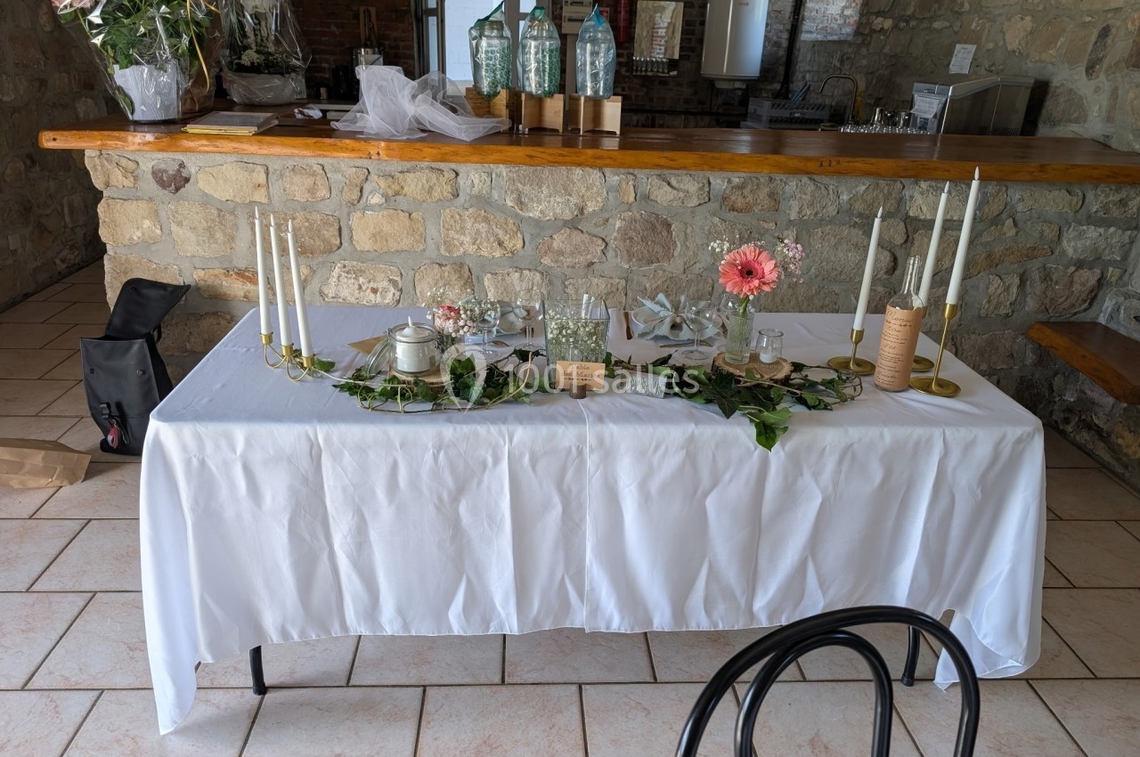 Table décorée avec nappe blanche, bougies, fleurs et éléments végétaux dans un intérieur en pierre.