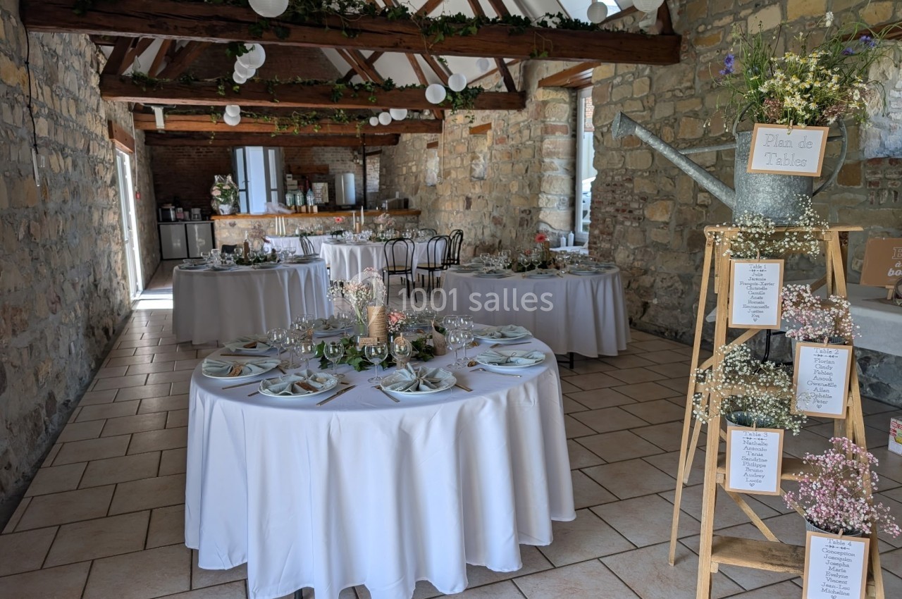 Salle de réception décorée pour un mariage, avec tables rondes dressées et guirlandes végétales suspendues.