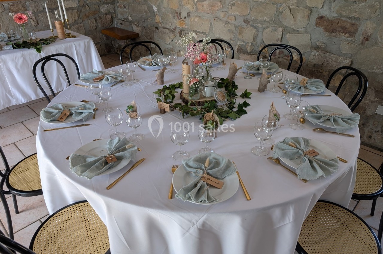 Table ronde décorée pour un repas, avec nappes blanches, serviettes pliées, couverts dorés et centre de table floral.