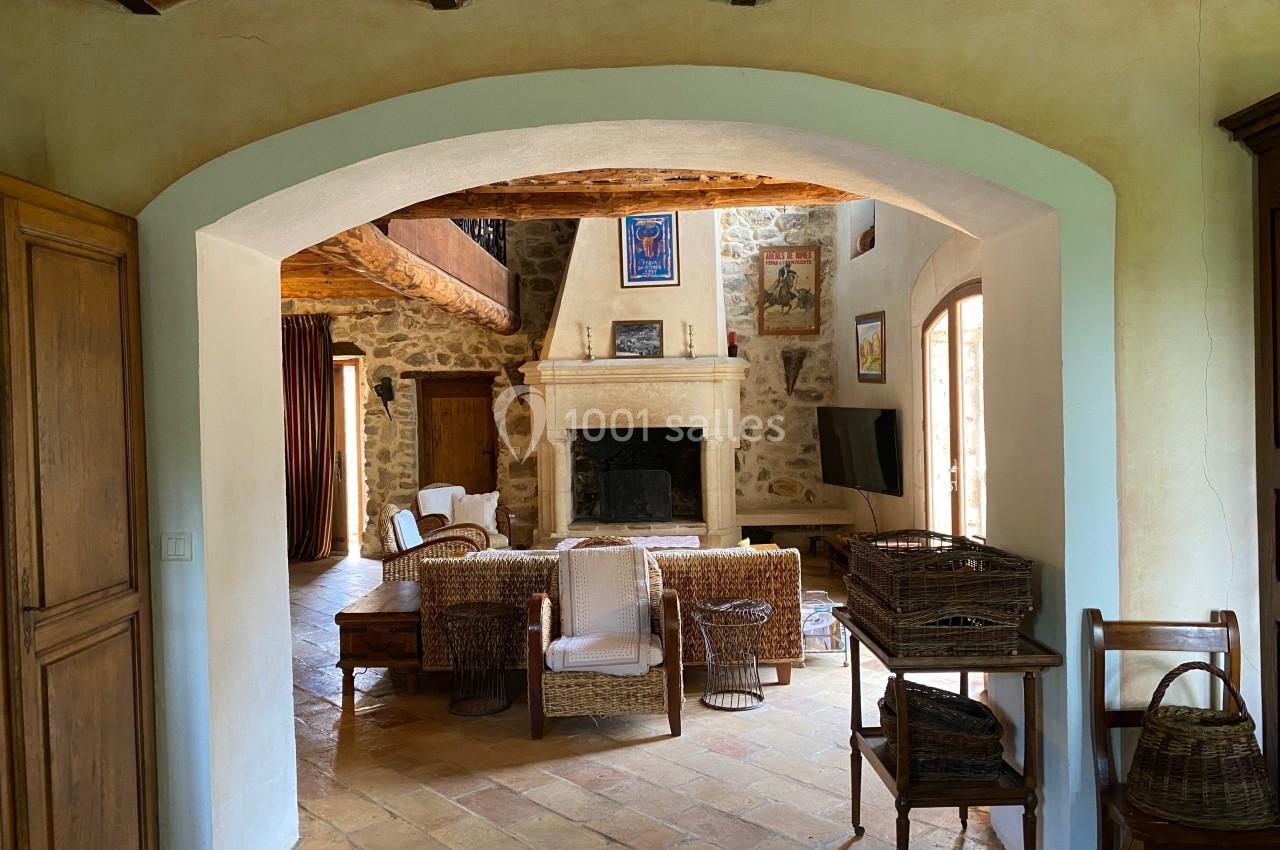 Salon rustique avec cheminée en pierre, poutres apparentes, mobilier en osier et sol en terre cuite.