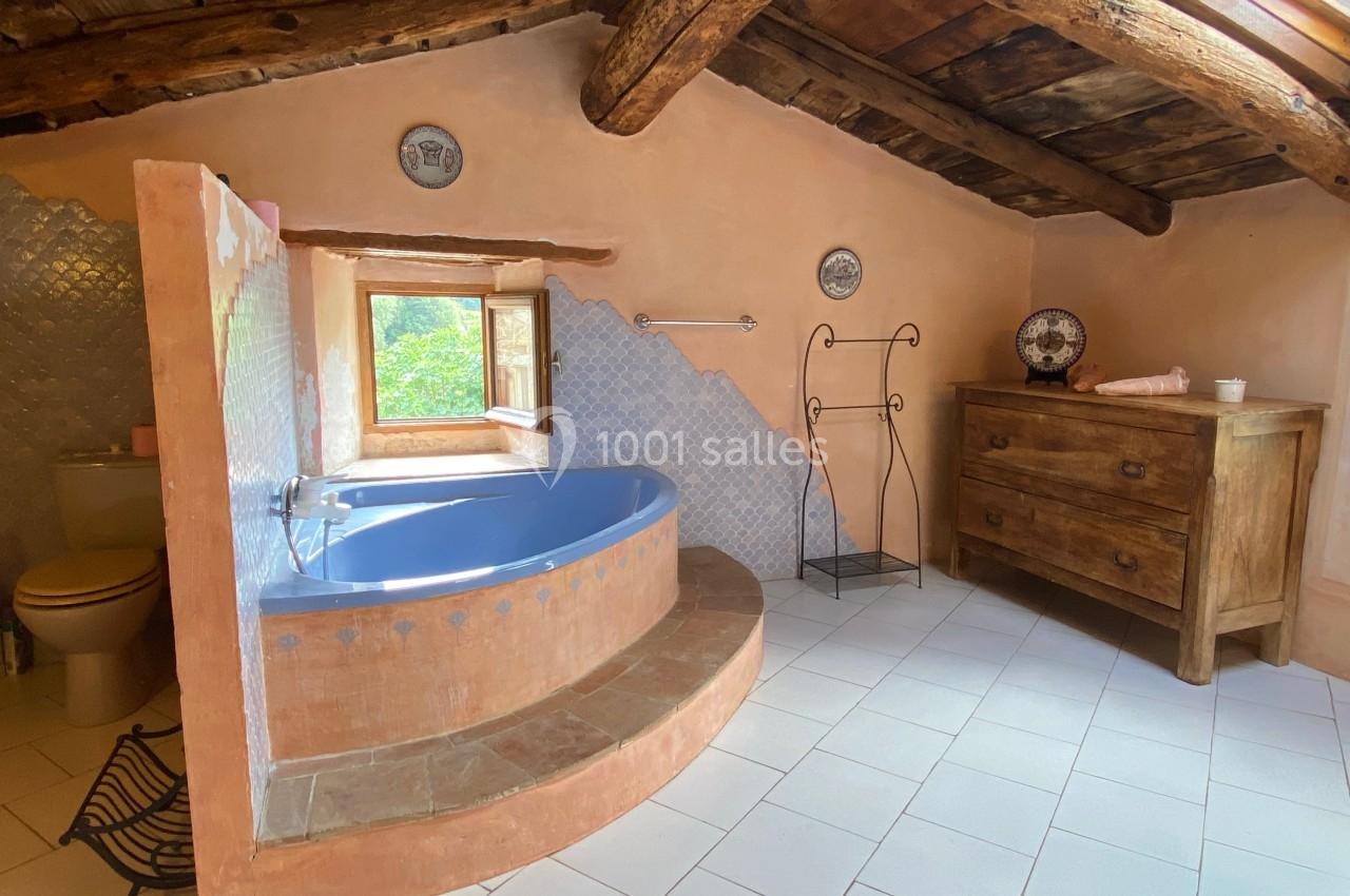 Salle de bain rustique avec baignoire bleue encastrée, poutres en bois apparentes et mobilier en bois ancien.
